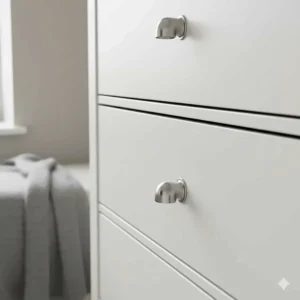 Close-up of brushed chrome cup handles on a white painted tallboy chest of drawers.