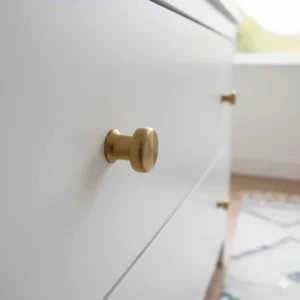 Close-up of brushed gold handles on a grey chest of drawers for a baby's room.