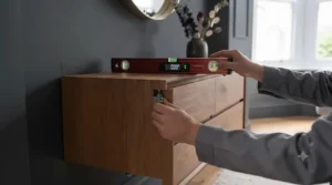 DIY step showing a spirit level being used to ensure a wall-mounted chest of drawers is hung straight.