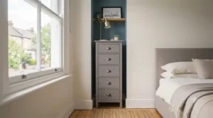 A tall, narrow slim chest of drawers fitting into a compact alcove space in a modern British apartment bedroom.