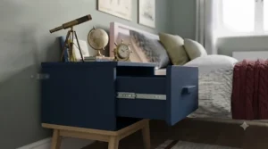 Deep navy blue 1 drawer children's bedside unit styled with storybooks and an alarm clock in an adventurous nautical-themed bedroom.