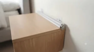 A demonstration image showing the innovative removable mounting hardware for a floating bedside storage shelf. The system allows for easy installation and clean, zero-damage removal, making it suitable for anyone living in a rented home.