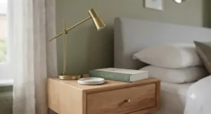 Narrow bedside table styled with a sleek brass reading lamp, a ceramic coaster, and a hardcover book.