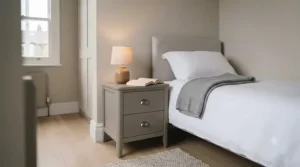 Compact grey bedside cabinet with drawers positioned neatly in a small guest bedroom with neutral walls.