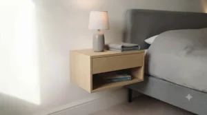 A practical, space-saving wall-mounted bedside cabinet in light oak, securely fixed at an accessible height next to a bed frame. The enclosed drawer and open shelf provide versatile storage for a small bedroom.